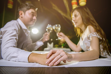 Asian couple holding hands together and cheering glasses of wine. Focus at hand and ring.