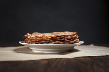 pancakes stacked in a plate on a dark wooden table on a dark gray background