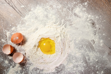 The top view of an egg, beaten into flour, cooking dough against the background of a wooden table. Flat lay