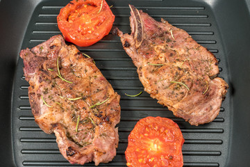 Grilled steak on grill pan with tomatoes on dark background