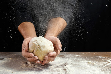 Male hands chef close-up, knead the dough, cook the dough on a dark background.