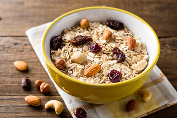 Oat flakes with nuts and dried fruits in bowl on dark wooden table