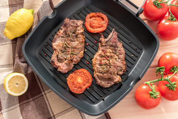 Grilled steak on grill pan with tomatoes and lemon on wooden background