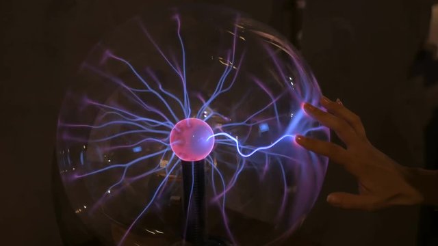 Interactive exposition in science museum. Woman touching plasma ball. Electricity and physics concept