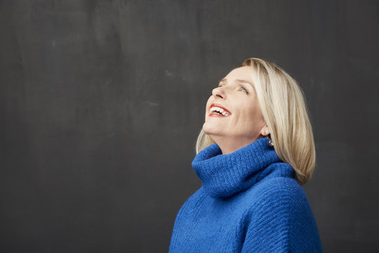 Overjoyed mature woman portrait. Studio shot of a laughing mature woman standing at isolated gray background. 