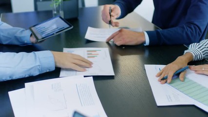 Moving Camera Flyover Shot of the Business Meeting Room Table with People Sharing Documents with Pie Charts and Statistics, Tablet and Laptop Screens. RED EPIC-W 8K Camera.