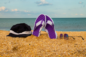 Pair of flip flops, hat and sunglasses on a sandy sea beach
