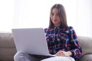 Girl holding netbook on hips while sitting on sofa