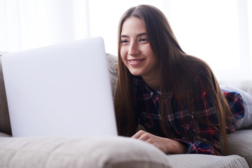 Smiling student surfing net while lying on sofa