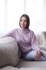 Girl wearing cozy sweater sitting on sofa at home, enjoying leisure time