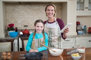 Smiling mother and daughter using digital tablet while preparing