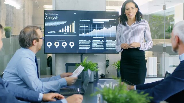 Beautiful Businesswoman Gives Report/ Presentation to Her Business Colleagues in the Conference Room, She Shows Graphics, Pie Charts and Company's Growth on the Wall TV.  RED EPIC-W 8K Camera.