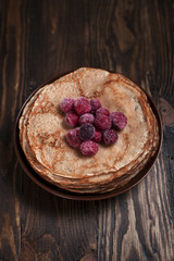 pancakes with frozen berries pile in a brown plate on a dark wooden table on a dark gray background