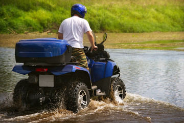 Man on ATV rides on the river, the view from the back.