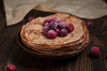 pancakes with frozen berries pile in a brown plate on a dark wooden table on a dark gray background