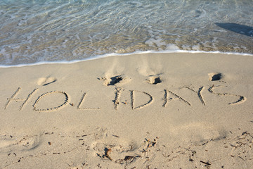 The word holidays written in the sand on a beach
