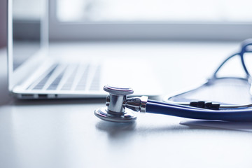 Stethoscope and laptop on doctor working desk with blurred focus for background, business and health care concept