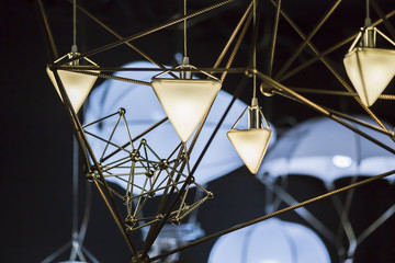 Modern chandelier in the form of a triangle and metallic geometric shapes, on a black background