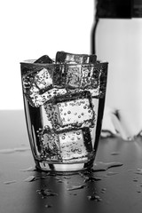 A glass of water with ice cubes on a wet surface