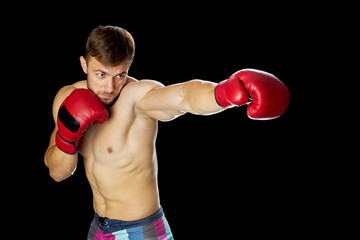 Fototapeta na wymiar Young boxer in red gloves. Athletic man throwing a pushing punch. Boxing classes concept.