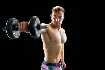 Fototapeta na wymiar Build muscle and gain strength. Strong guy with sculpted torso lifting dumbbells on black.