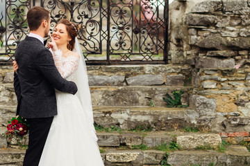 the groom holds a wedding bouquet in one hand, and in the other hand hugs his wife behind the waist