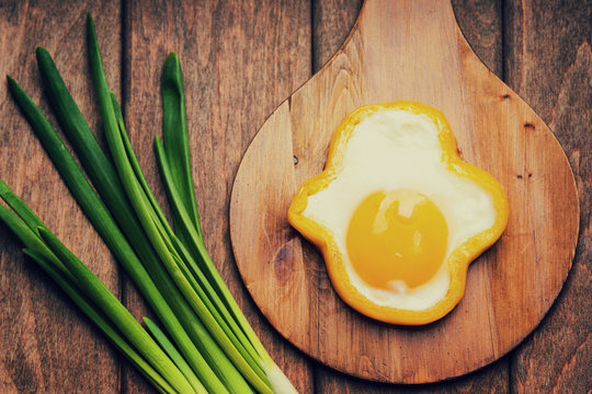 Bell pepper egg ring on a cutting wooden board and green onion 