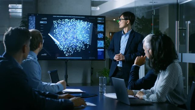 In the Conference Room Chief Engineer Presents to a Board of Scientists New Revolutionary Approach for Developing Artificial Intelligence and Neural Networks. Wall TV Shows Their Achievements.