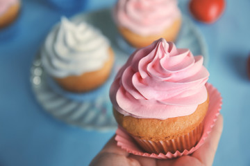 Woman holding tasty cupcake on blurred background, closeup