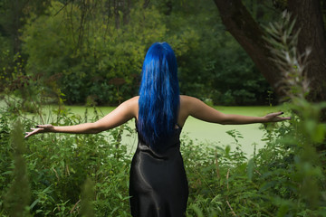 Beautiful woman with dark blue hair dressed in black dress in the magic forest