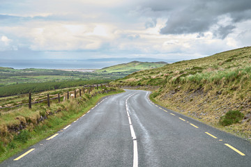 Distant view of a road leading to a town with a beach port and mountains. Beautiful landscape and fields. Ring of Kerry, Ireland.