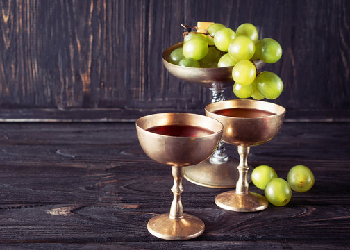 Antique golden goblets with red wine and bunch of grapes, vintage lifestyle