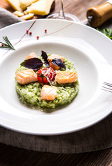Risotto with basil and salmon in a white plate on a dark wooden background top view