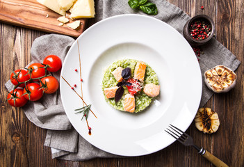 Risotto with basil and salmon in a white plate on a dark wooden background top view