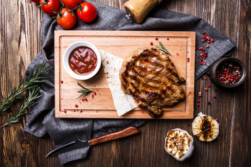 Fototapeta na wymiar Juicy grilled steak with tomato sauce on a board on a dark wooden background top view