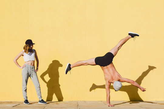Couple doing acrobatics in front of a yellow wall.