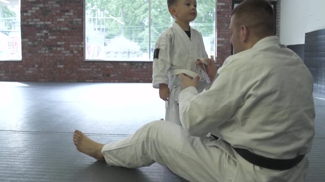 Instructor tying a belt of a boy in a dojo