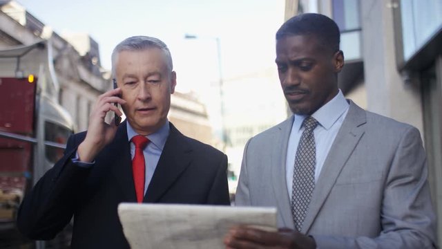 Two male investors talking on the phone as they walk and check share prices