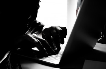 Hackers with black mask using hands of anonymous typing code on keyboard of laptop for remotely...
