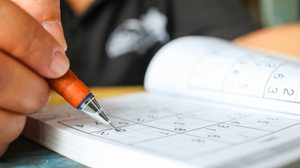 Student  is trying to solve sudoku with  color pencil as hobby at outdoor
