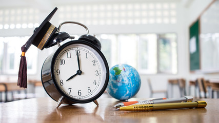 Retro alarm clock 2 o'clock, left side on table teacher with earth global map, Graduation cap, pen...