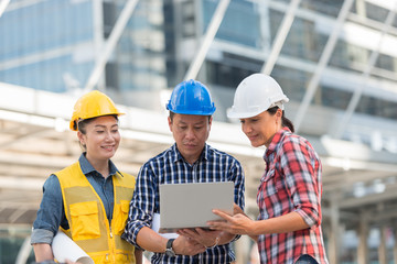 Asian engineers group consult construction on site building working while holding laptop and blueprint paper. in city background. teamwork concept.