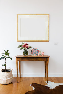 Blank picture frame above a side table with flowers and pot plant