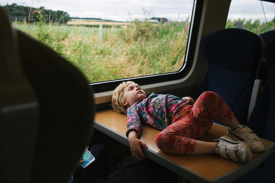 A girl lies down on a table on a train during a long journey.