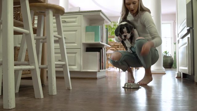Young woman feeding a puppy with dog food in a kitchen