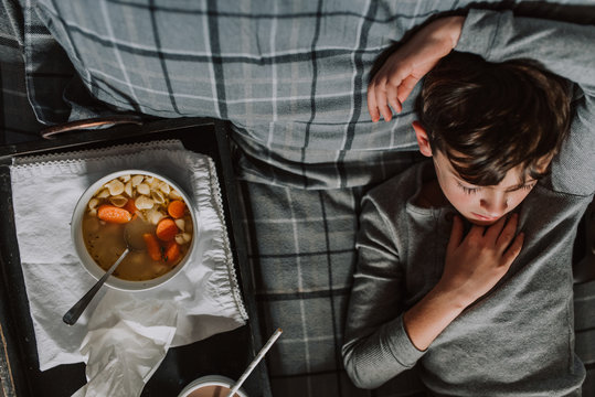 Boy with flu lying in bed with chicken soup
