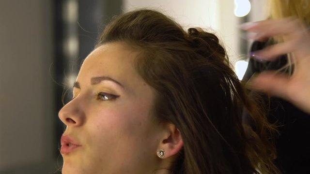 Young beautiful girl in beauty salon. Hairdresser-stylist makes the girl's hair. The hairdresser curls the hair with a styler and stacks them.