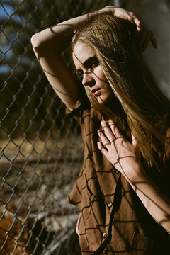 Woman Standing in Front of a Fence with Shadows and Harsh Light on Her Face