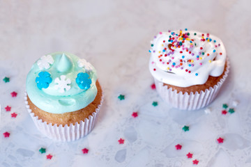 Two cupcakes with cream and pastry decorations on a light background.