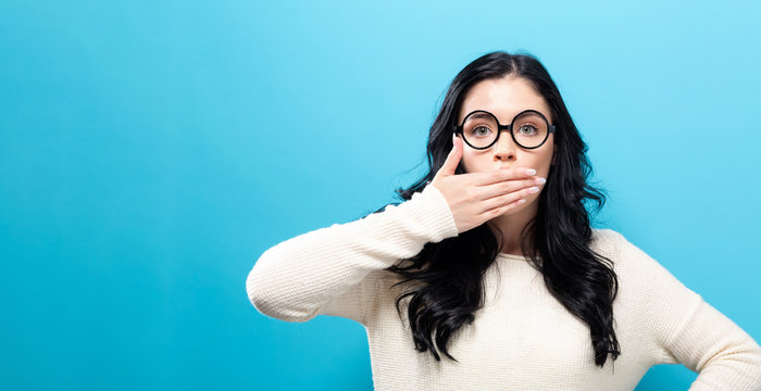 Young woman covering her mouth on a solid background